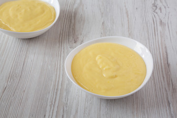 Homemade vanilla custard pudding in bowls over white wooden background , low angle view. Close-up.
