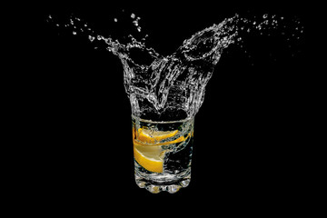 Two slices of lemon dropped into a glass of water on black background