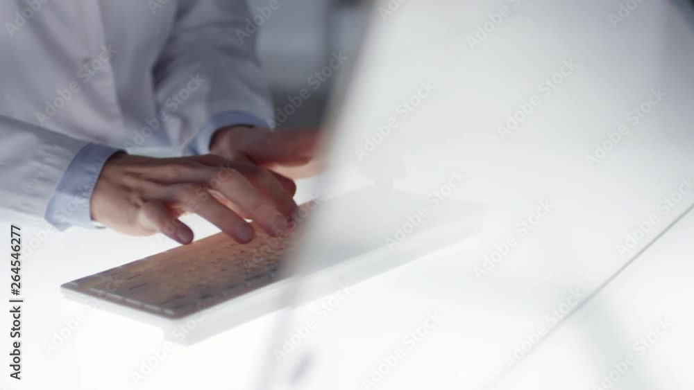 Poster close up tracking shot of hands of female doctor in lab coat typing on modern wireless keyboard whil