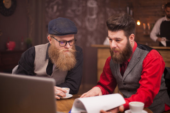 Two Bearded Collegues Working Together On A Computer In A Coffee Shop