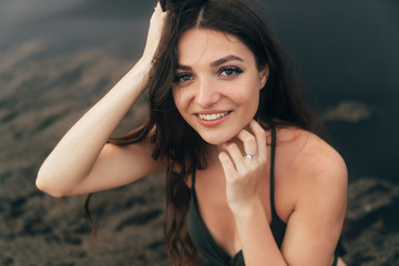 Portrait of happy girl with beautiful smile in swimsuit posing on black sand beach