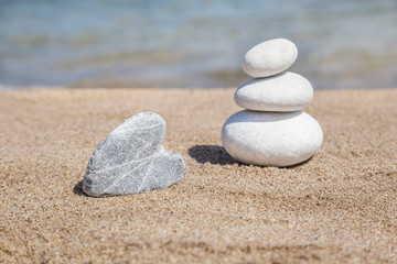 Fototapeta na wymiar heart shaped stone and stack of pebbles on balance on sandy beach