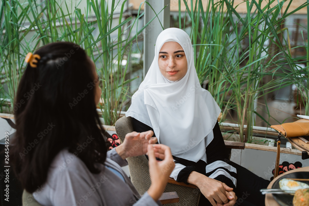 Wall mural muslim woman talking in cafe together. girl with scarf having a chat