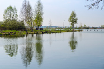 Fototapeta premium A place for meditation-wooden gazebo stands on the shore of the Lake near the young trees