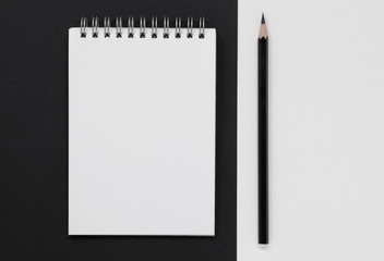 Open blank notepad with a black pencil on a black and white background.