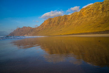 Spain, Lanzarote, Huge mountains of famara massif reflected in famara beach at sunset