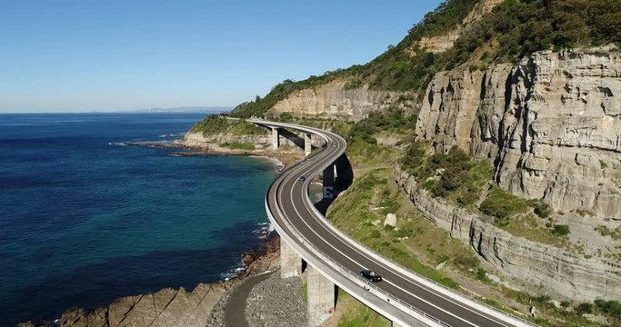Small passenger convertible car driving of the Grand Pacific Drive road &ndash; Sea Cliff bridge at the edge of Pacific ocean. Elevated aerial view of traffic.