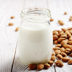 Obraz na płótnie Canvas Milk or yogurt in mason jar on white wooden table with almonds aside