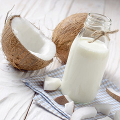 Glass bottle of milk or yogurt on blue napkin on white wooden table with coconut aside