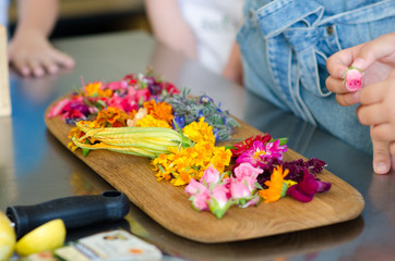 Obraz na płótnie Canvas Cut edible flowers on a wooden cutting board. People are preparing to make dishes. It can be workshops for children and adults.
