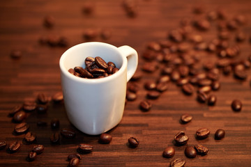 An espresso cup on a table filled with and surrounded by roasted coffee beans