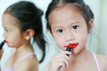 Adorable little Asian child girl trying mother's lipstick near a mirror.