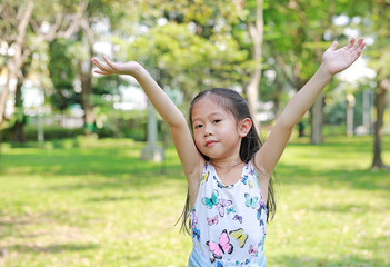 Happy little Asian child girl opened her hands in the summer park.