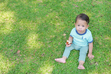Asian baby boy enjoy eating fried chicken in the green garden outdoor.