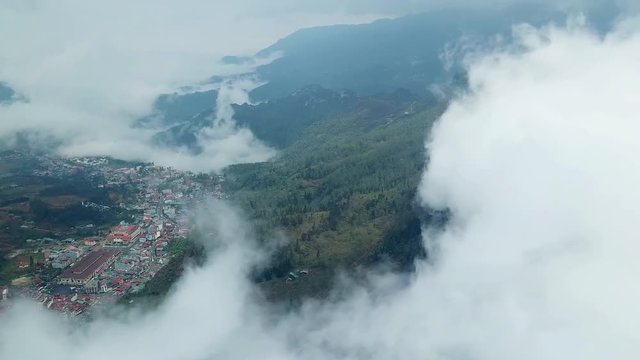 Helicopter high dark mountains in clouds of fog. Smoke. Sharp peaks. Epic natural landscape. Old village  Sapa countryside houses. Spruce forest on slopes. Mainly cloudy. Asia Europe. Aerial drift