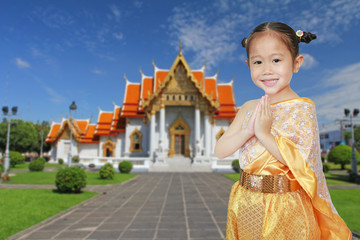 Portrait of asian child girl in traditional thai dress praying against Benjamaborphit temple in thailand.