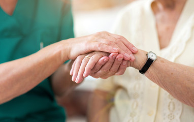 Nurse consoling her elderly patient by holding her hands
