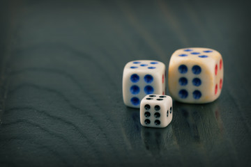 three dice of different sizes on a dark blurred background. toned. space for text