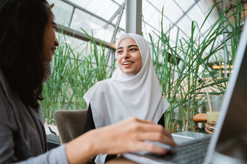 muslim woman and friend discussing with laptop. student learning in cafe
