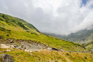 The Transfagarasan road in Fagaras mountains, Carpathians with green grass and rocks, peaks in the clouds