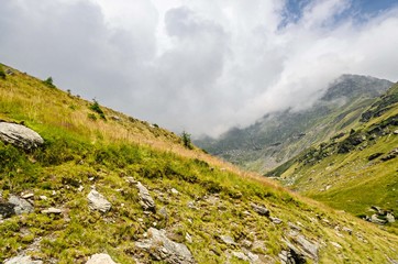 Fototapeta premium The Transfagarasan road in Fagaras mountains, Carpathians with green grass and rocks, peaks in the clouds