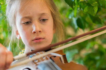 Close up of a child playing violin on green background. Portrait of girl with string and playing...