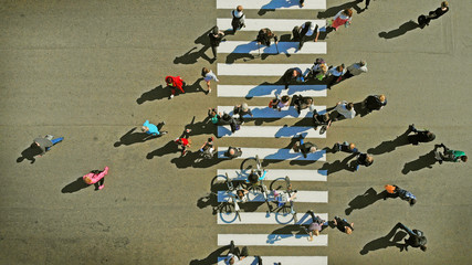 Aerial. People crowd on pedestrian crosswalk, top view. Cyclists among the crowd.