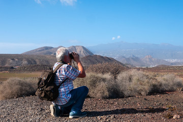 Senior man with white hair stop and have a look with a binocular during an excursion