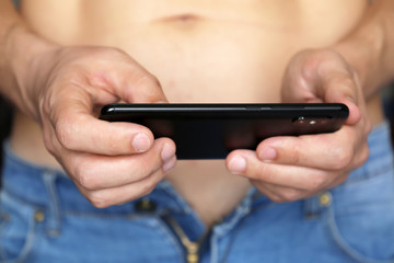 Sporty man in unzipped jeans with smartphone in his hands. Concept of watching porn video, playing...