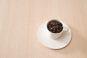 Cup of full coffee beans on the wood background