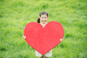 草原でハートを持ち微笑む女の子
