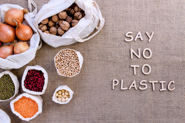 Reusable shopping bags on background of burlap. Wooden letters with inscription say no to plastic. Ecological pouches with .chickpeas, hazelnuts, beans, lentils, onions, nuts. Zero waste concept.