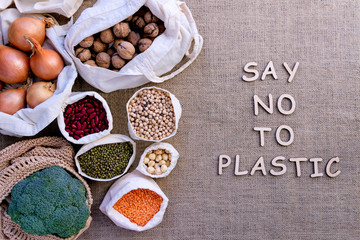 Reusable shopping bags on background of burlap. Wooden letters with inscription say no to plastic. Eco pouches with .chickpeas, hazelnuts, beans, lentils, onions, nuts, broccoli. Zero waste concept.