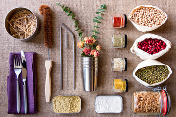 Natural washing agents, accessories, reusable packages for using in kitchen laid out geometrically correctly, in rows. Coconut brush, metal straws, cotton bags on burlap background. Zero waste concept