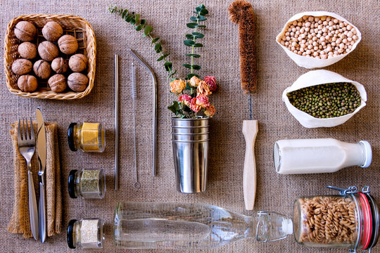 Reusable natural ecological packages and containers, coconut brush, metal straws for using in kitchen laid out geometrically correctly, in rows on burlap background. Zero waste, plastic free concept.