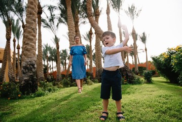 Obraz premium Stylish mother and handsome son having fun on a green lawn. Happy family concept. Beauty nature scene with family outdoor lifestyle. Happy family resting together. Mothers day