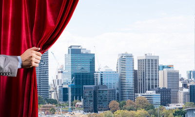 Modern business cityscape behind curtain opened by businessman hand