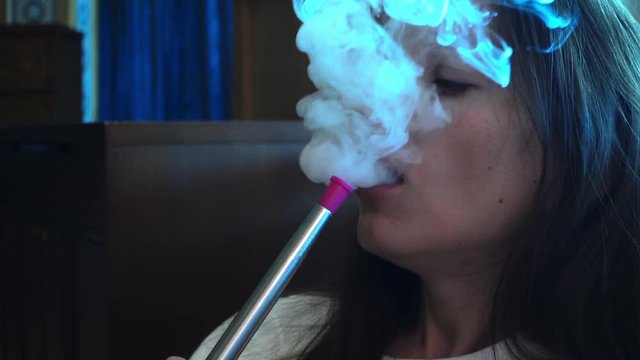 Smoking is harmful to health. Restaurant Teahouse with hookahs. The girl smokes a hookah through her nose. Smoke slowly comes out of the nose