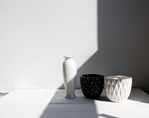 Vase, black-and-white pots on wood table. White wall, background with sunlight and shadows. Modern interior. Minimalism style.