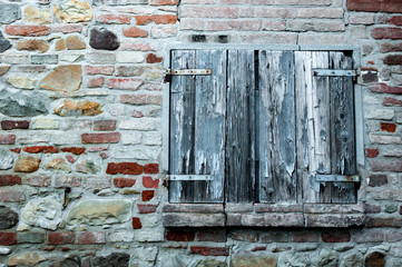 Window shutter of rural house, with brick wall and ancient stones.