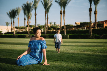Fototapeta premium Stylish mother and handsome son having fun on a green lawn. Happy family concept. Beauty nature scene with family outdoor lifestyle. Happy family resting together. Mothers day