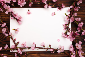 White paper sheet and sprigs of the apricot tree with flowers on wooden background. Place for text. The concept of spring came, happy easter, mother's day.Top view.Flay lay. Copy space.