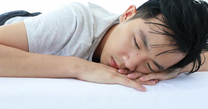 Asian man lie prone on bed, he in pajamas in bedroom.