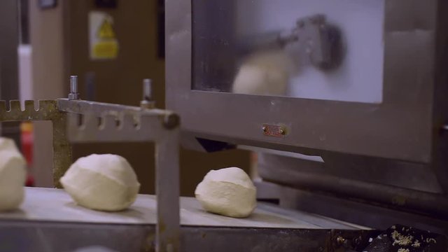 Rotating arm slicing bread dough into equal circles, falling onto a conveyor belt and moving out of shot