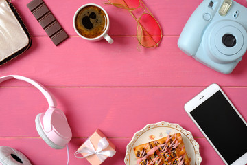 Composition with instant camera, smartphone, headphones, sunglasses, cup of coffee, tasty wafer cake on pink wooden background. Beauty blogger concept. Stylish hipster women desk. Flat lay. Top view.