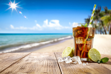 Fresh cold drink on wooden table and free space for your decoration. Summer blurred background of beach and palms with ocean landscape and sun . 