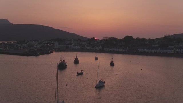 Video taking looking west over Ullapool village as the sunsets behind the Summer Isles.  Drone reveal shot from lochbroom ascending over Ullapool.  Ullapool is located on the NC500 / North Coast 500