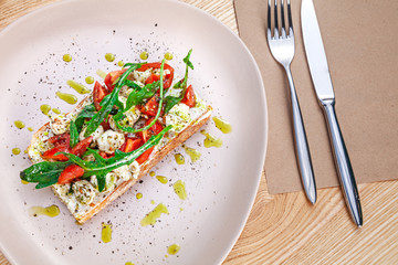 Top view on bruschetta with mozzarella, cherry tomatoes and arugula served on plate on wooden table. View from above on flat lay food for lunch. Healthy snack. Copy space for design. Italian cuisine
