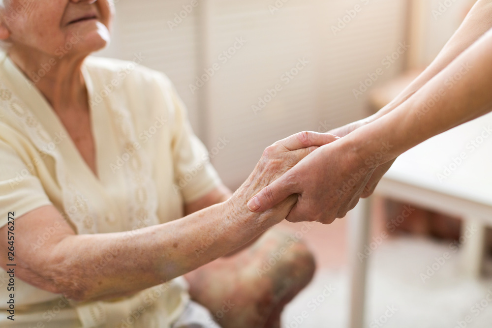 Poster nurse consoling her elderly patient by holding her hands