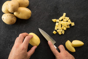 Hand cutting potatoes on textured black background.